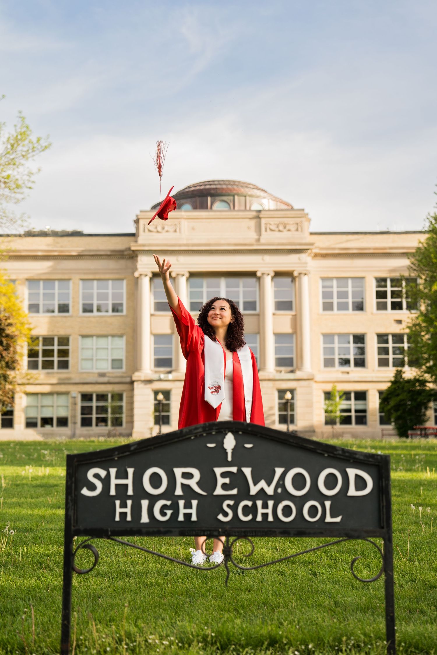 Photo of a girl tossing her cap in front of a school during cap and gown session taken by Milwaukee event photographer Rachel Dickman.