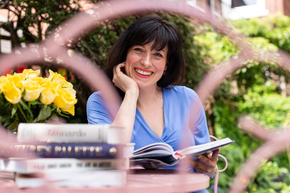 Reading outdoors at a garden table with yellow flowers and a book in a peaceful setting.