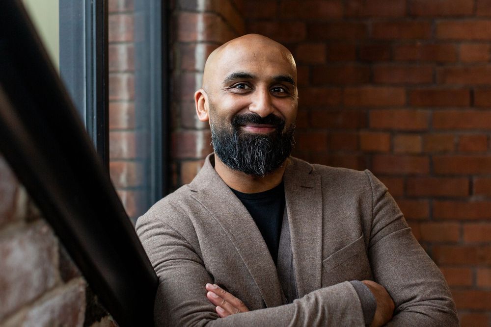 Professional wearing a brown suit jacket poses against brick wall in multiple candid shots.