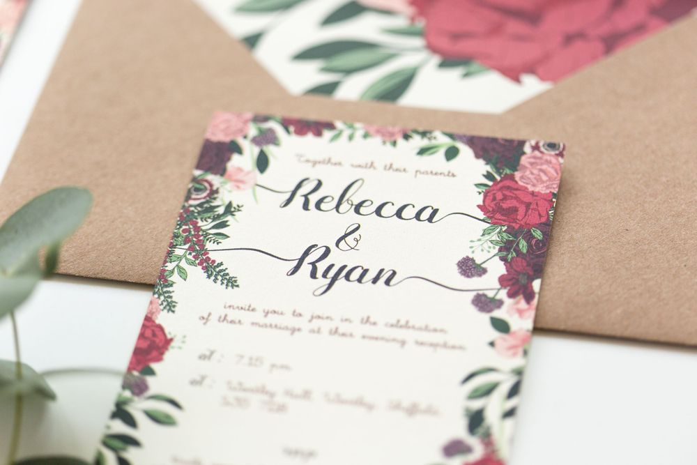 Wedding invitation with pink and purple floral border design on white paper.
