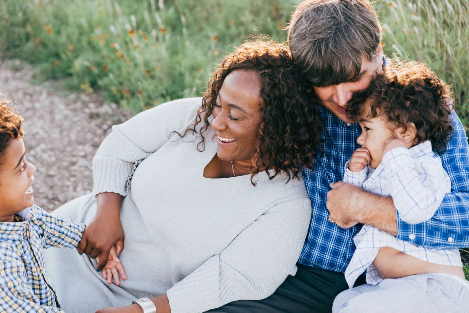 A diverse family sits together outdoors on a dirt path, sharing laughter and smiles in natural lighting.