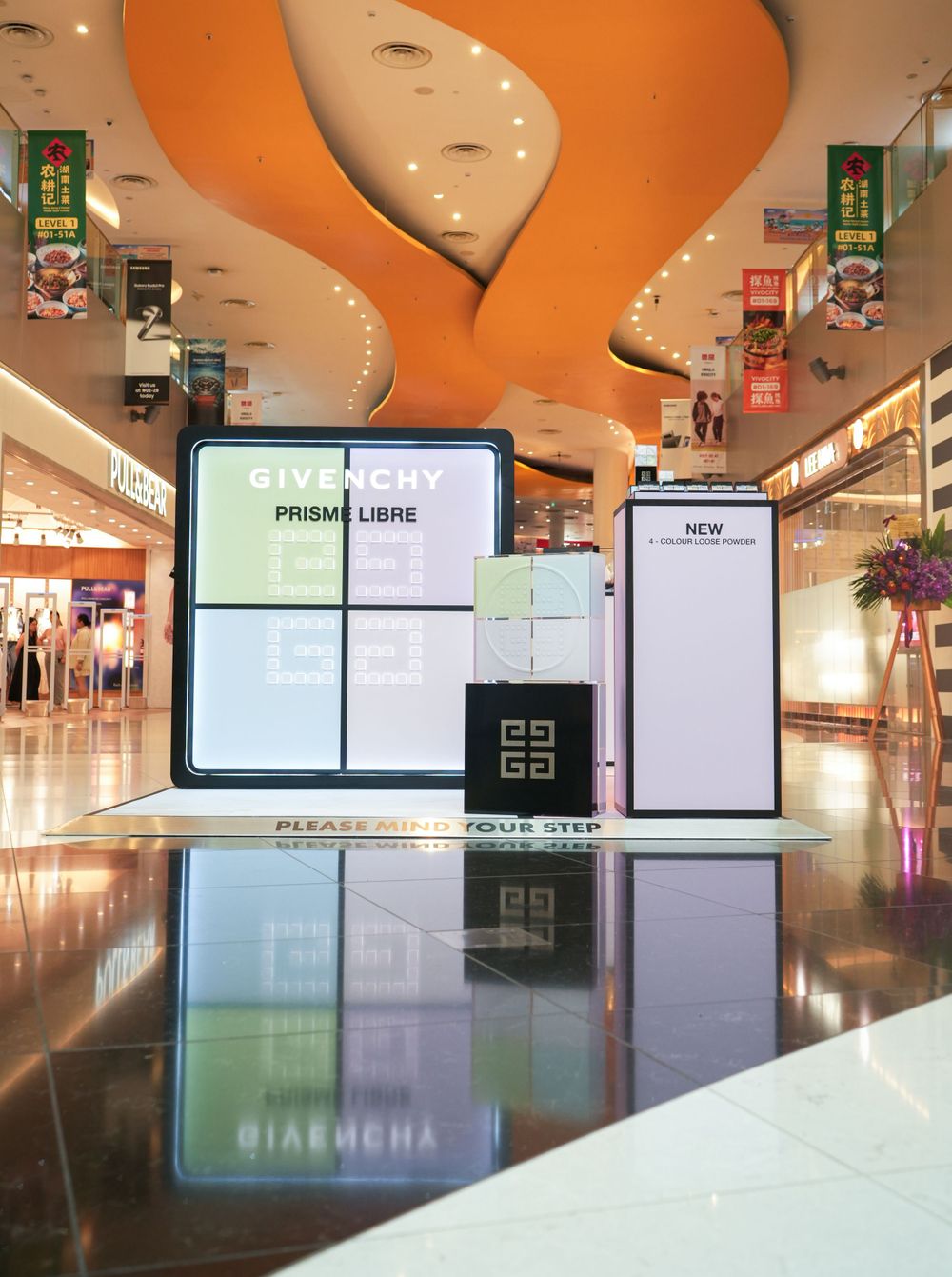 Modern shopping mall interior with curved orange ceiling design and illuminated digital displays.