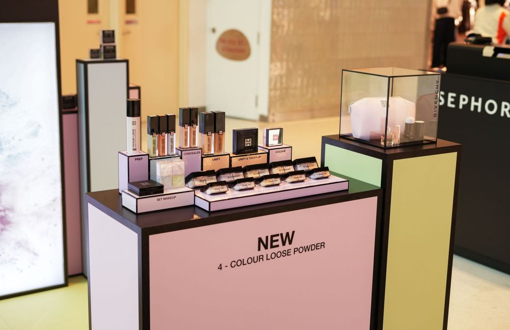 Modern cosmetic retail display featuring new products on a pink platform with tiered shelving.