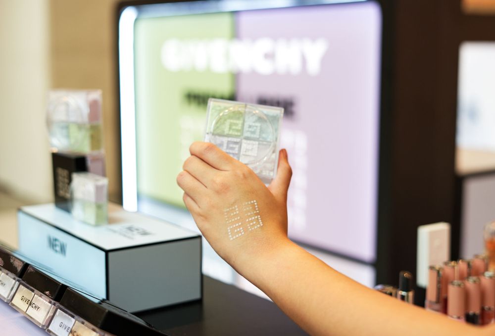Hand holding up a Givenchy makeup product against a display screen.