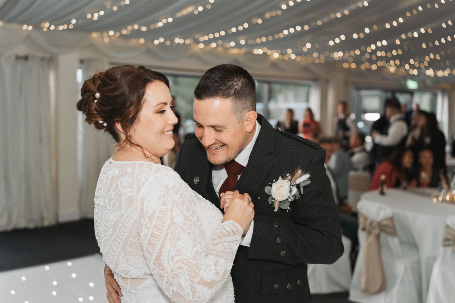 A couple shares an intimate moment while dancing together at their wedding reception under twinkling string lights.