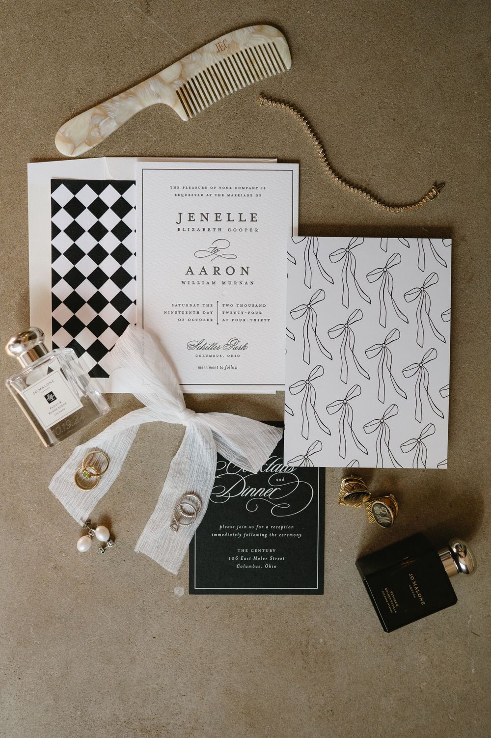 Modern black and white wedding invitation suite with checkered pattern and accessories on brown background.