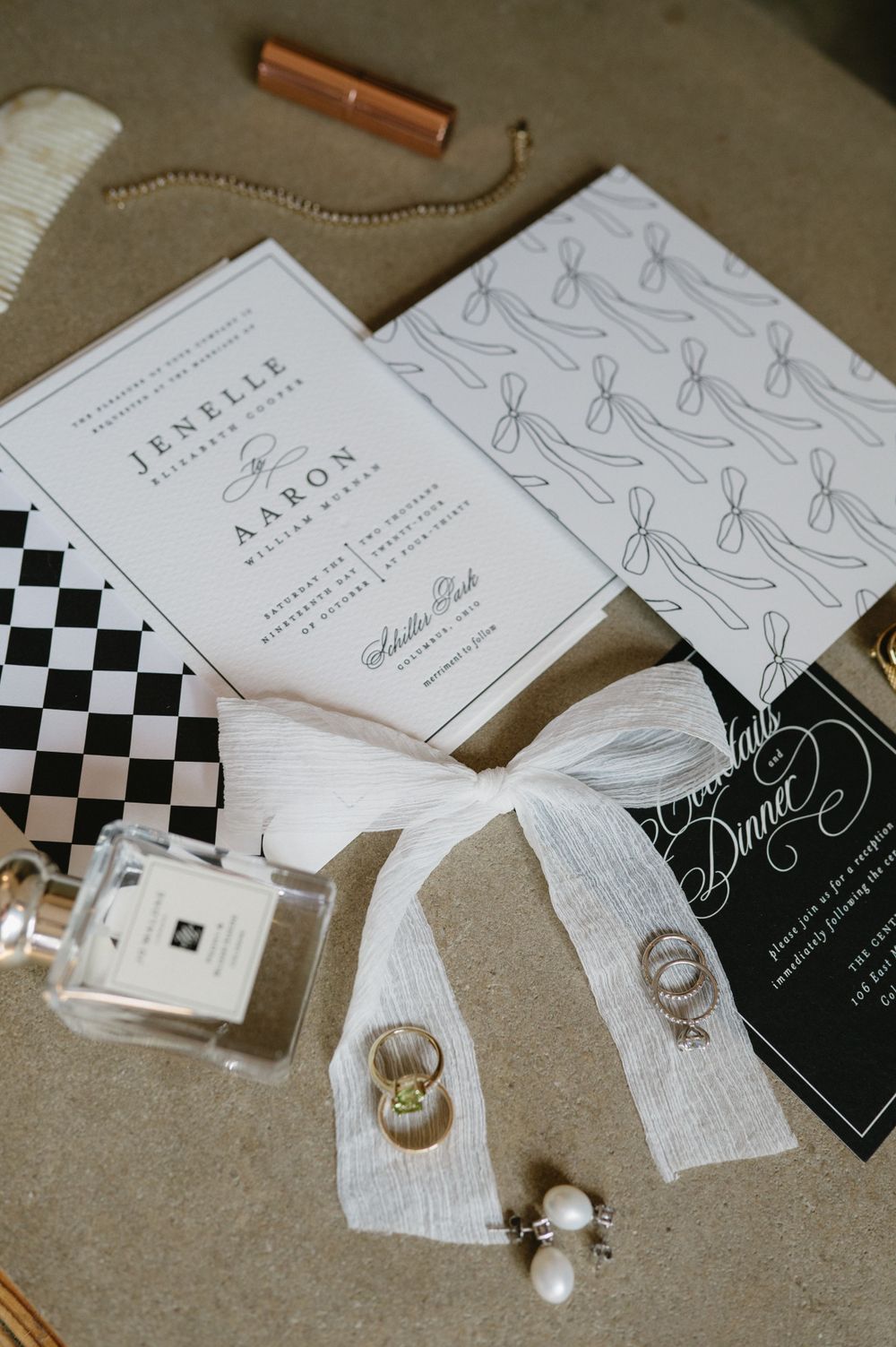 Wedding details including invitations, rings, and perfume bottle arranged on neutral background.