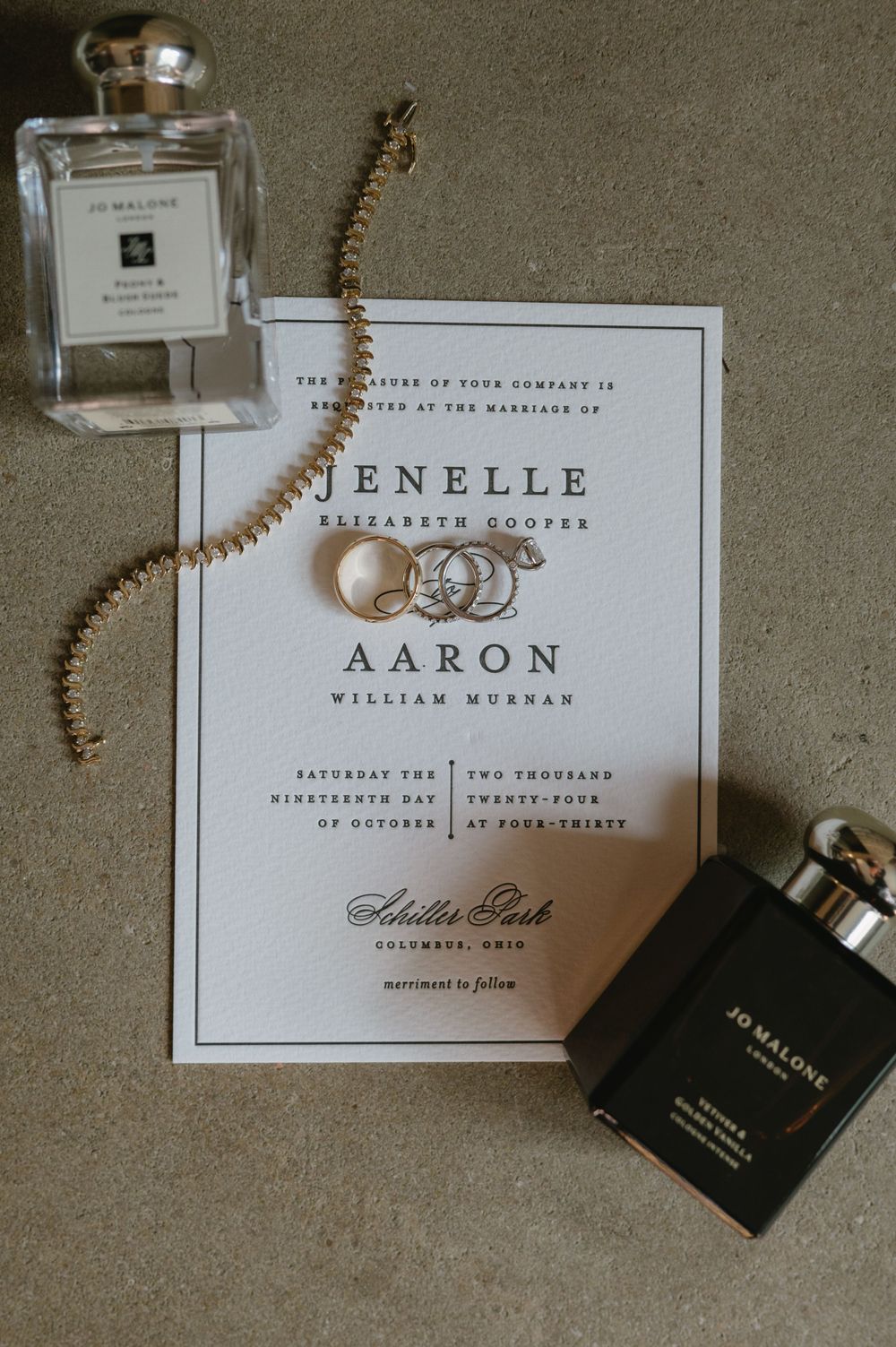 Elegant wedding invitation with couple's names displayed with Jo Malone perfume and jewelry.