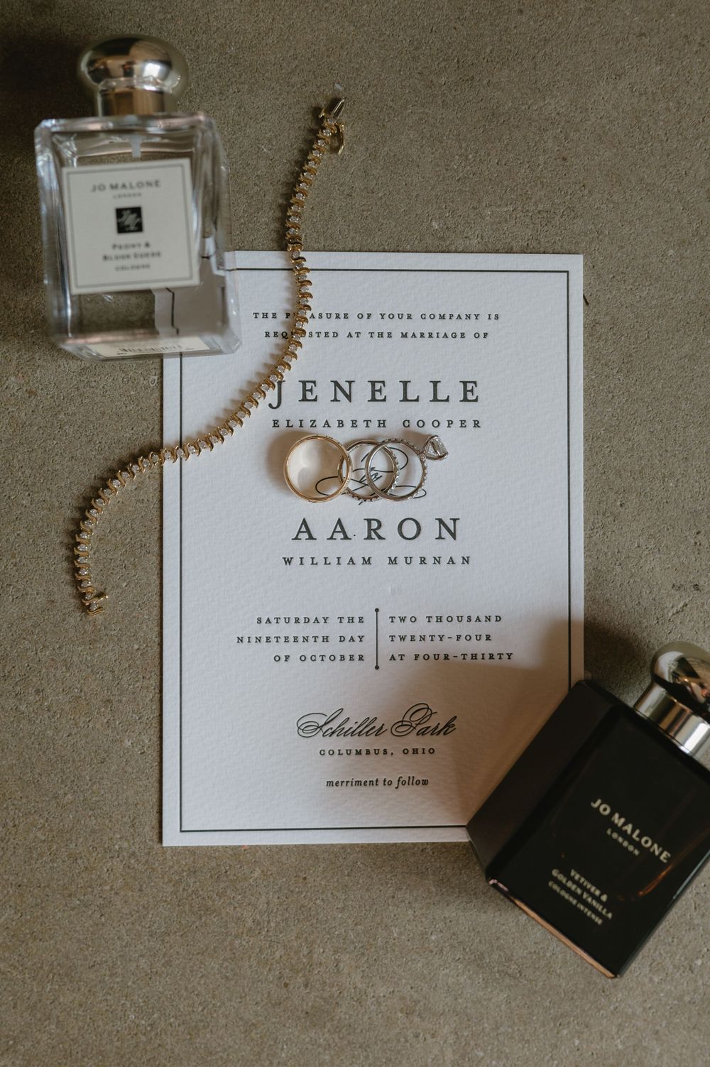 Minimalist wedding invitation flanked by luxury perfume bottles and delicate gold jewelry.