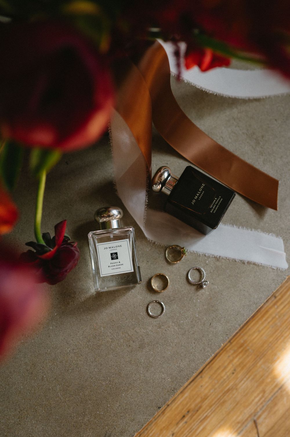 Wedding accessories including perfume bottles, rings, and red tulips arranged on a gray surface.