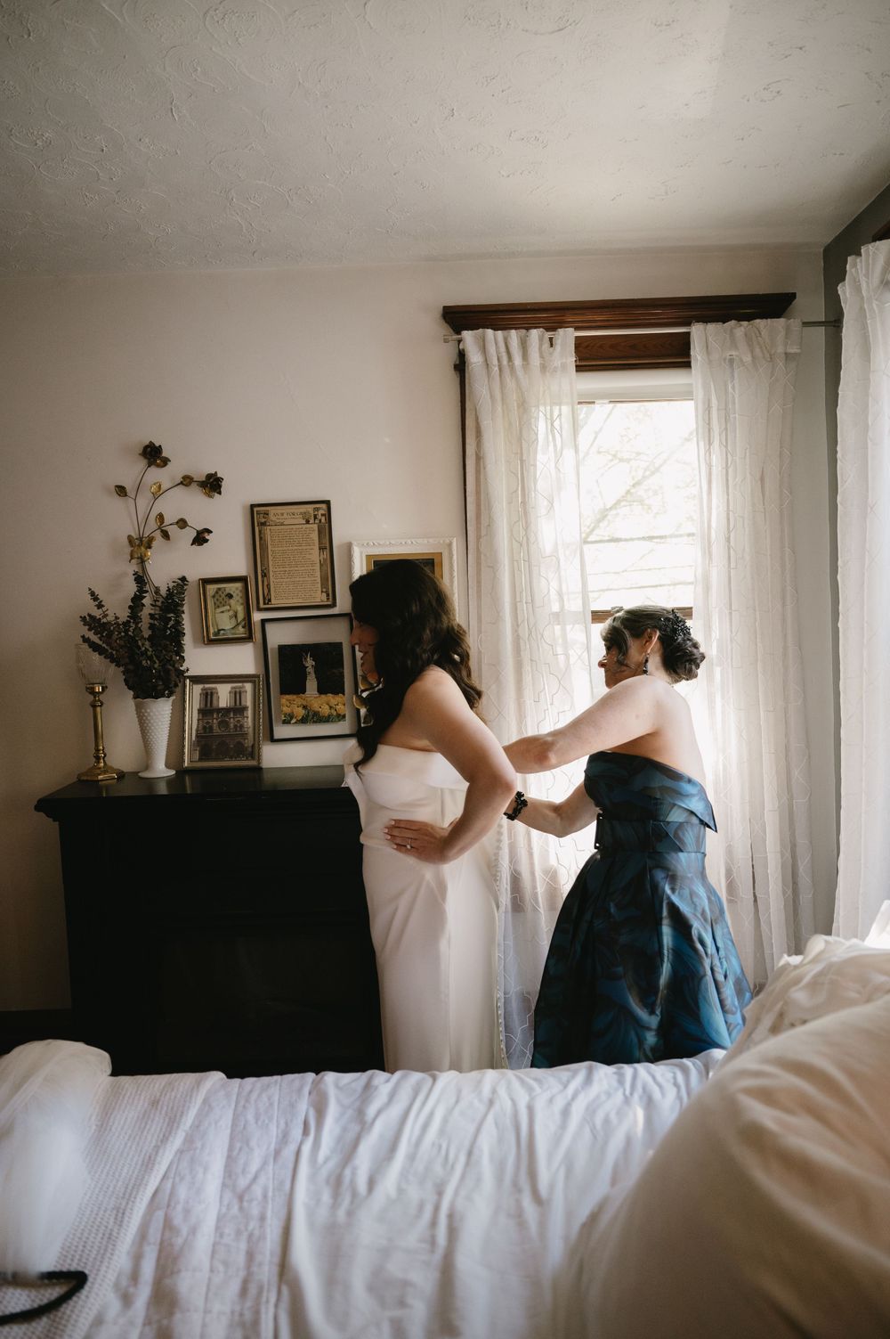 Getting ready scene in sunlit bedroom with white dress and navy gown preparations.