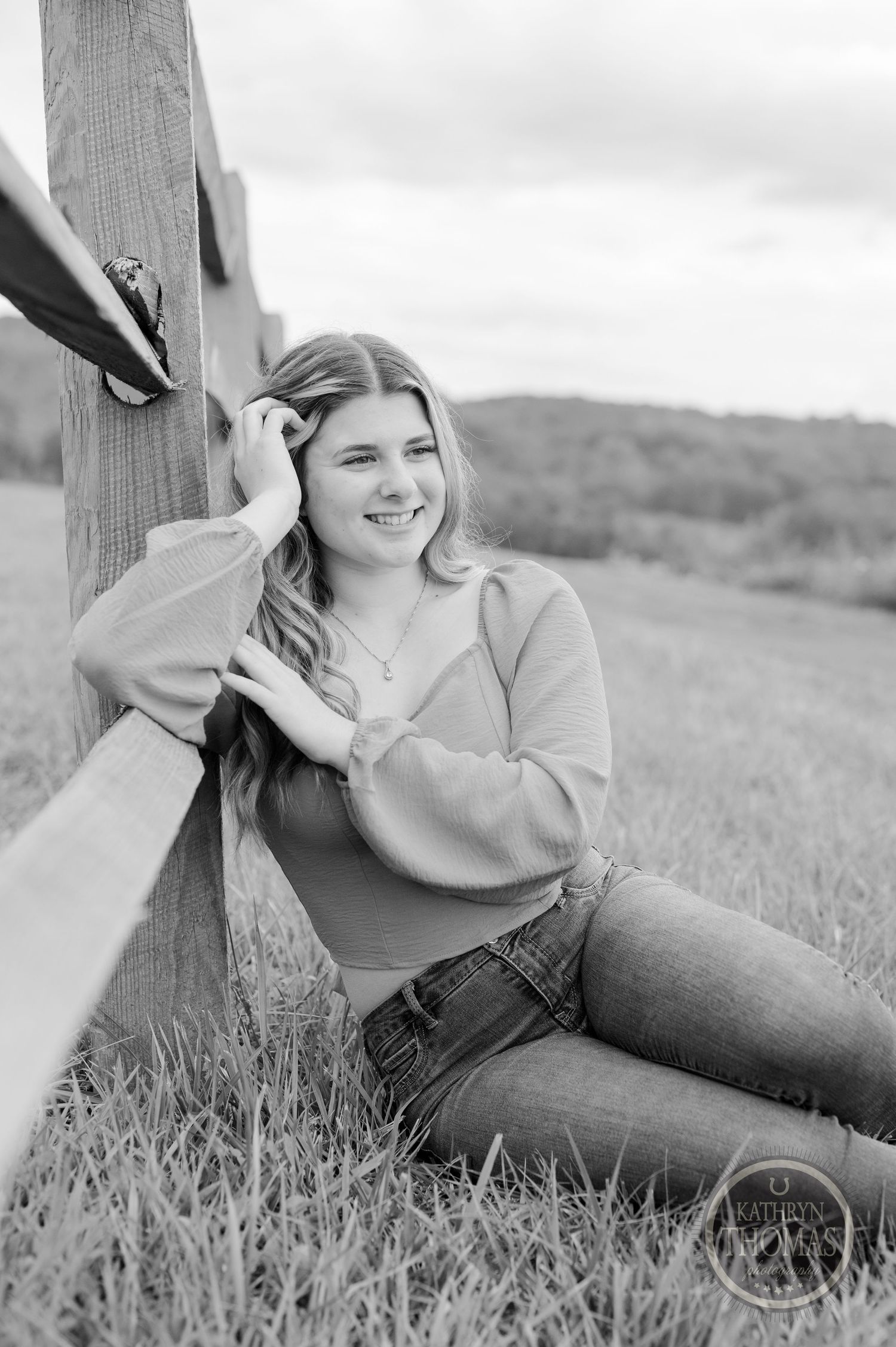Black and white portrait of someone reclining by wooden fence in casual attire.