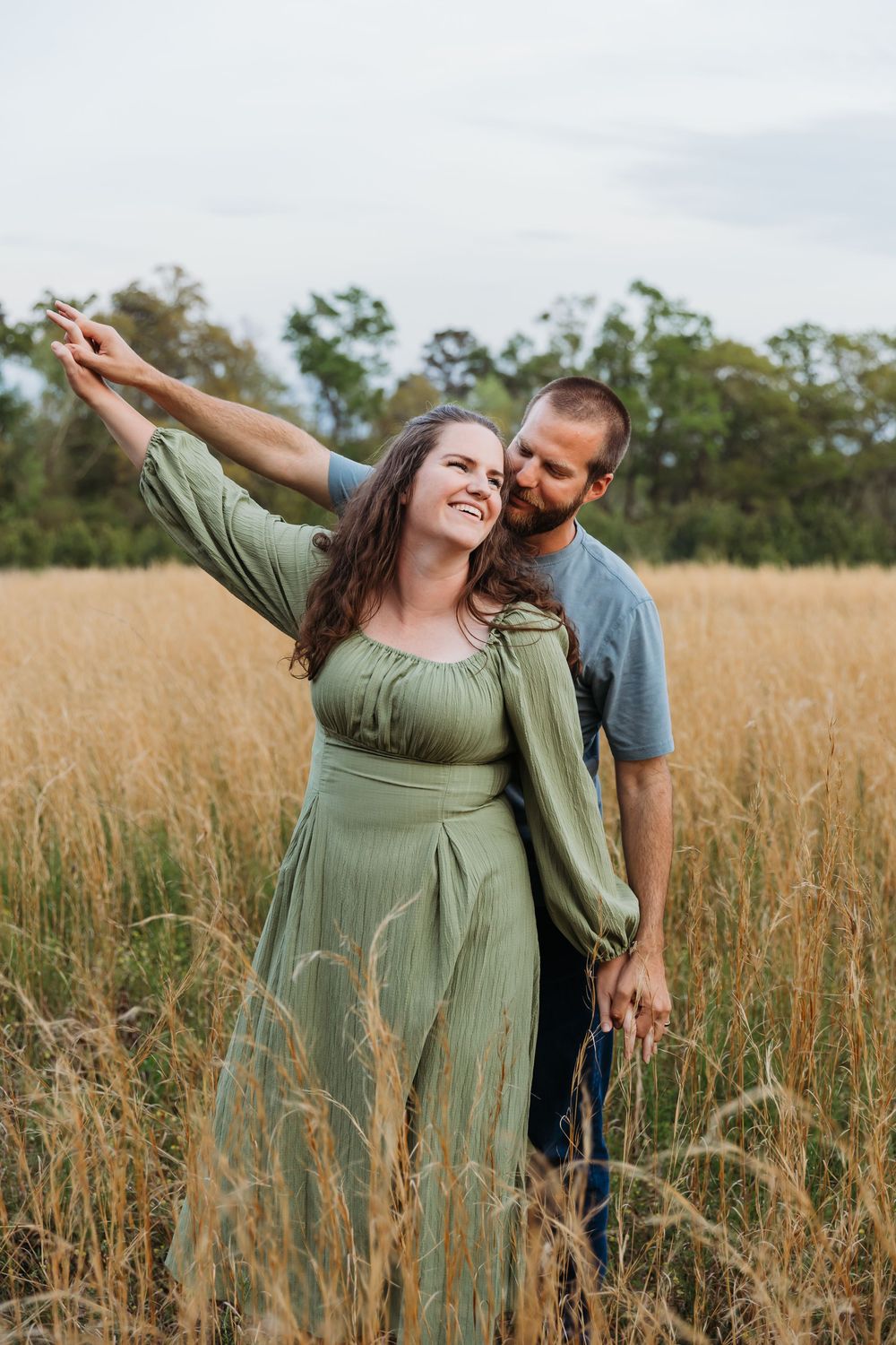 A couple shares a joyful moment dancing together in a golden wheat field during sunset.