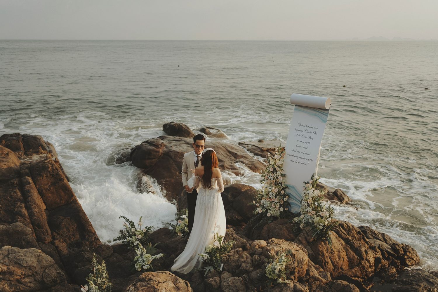 Coastal wedding scene with flowing white dress against rocky oceanside cliffs.