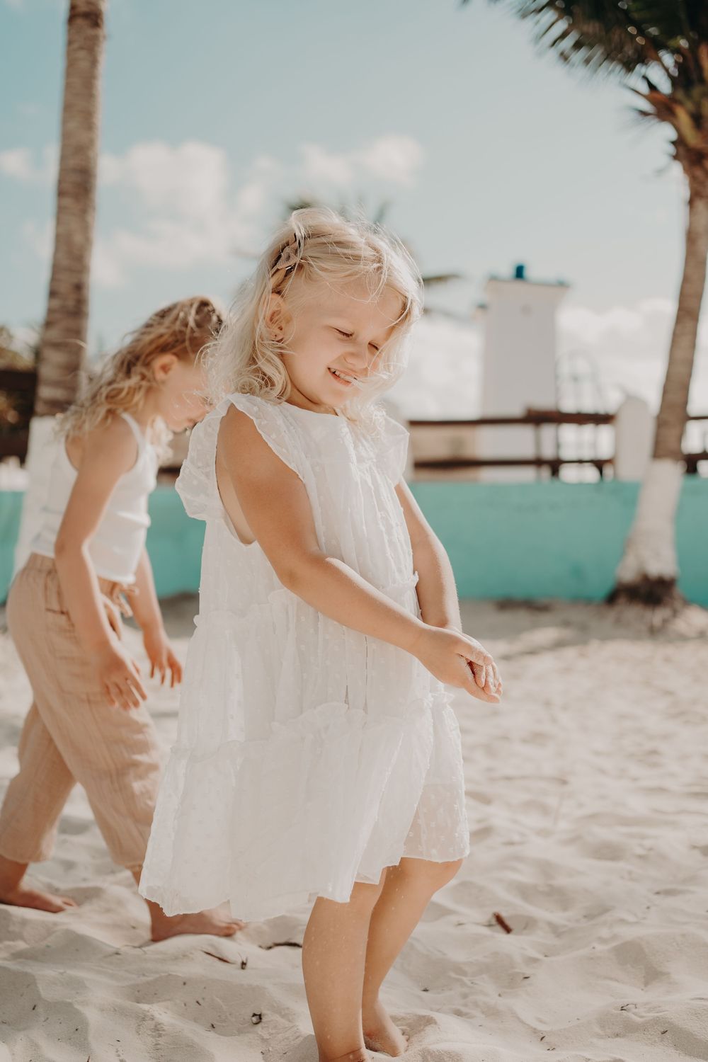Young children playing and dancing on a tropical beach with palm trees and white buildings photoshoot in Puerto Morelos.