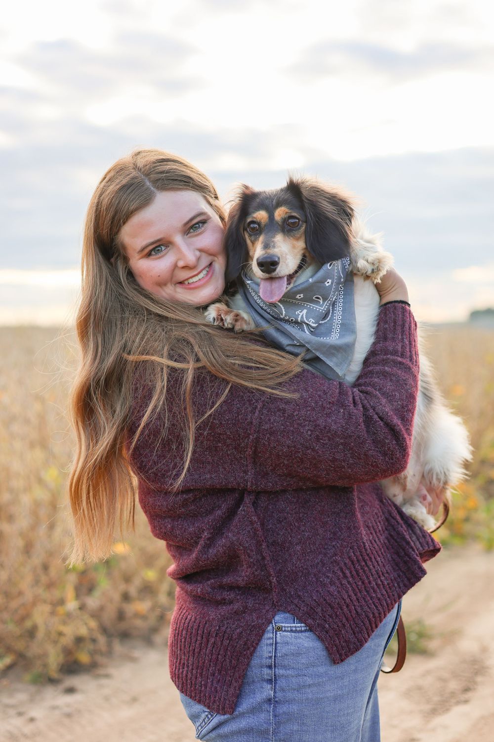 Girl holds multicolored dog with a blue bandana in a field