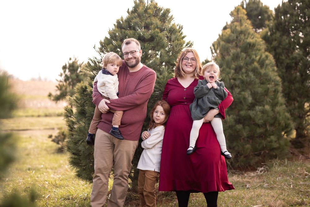 Family of 5 pose together and laugh in a tree farm
