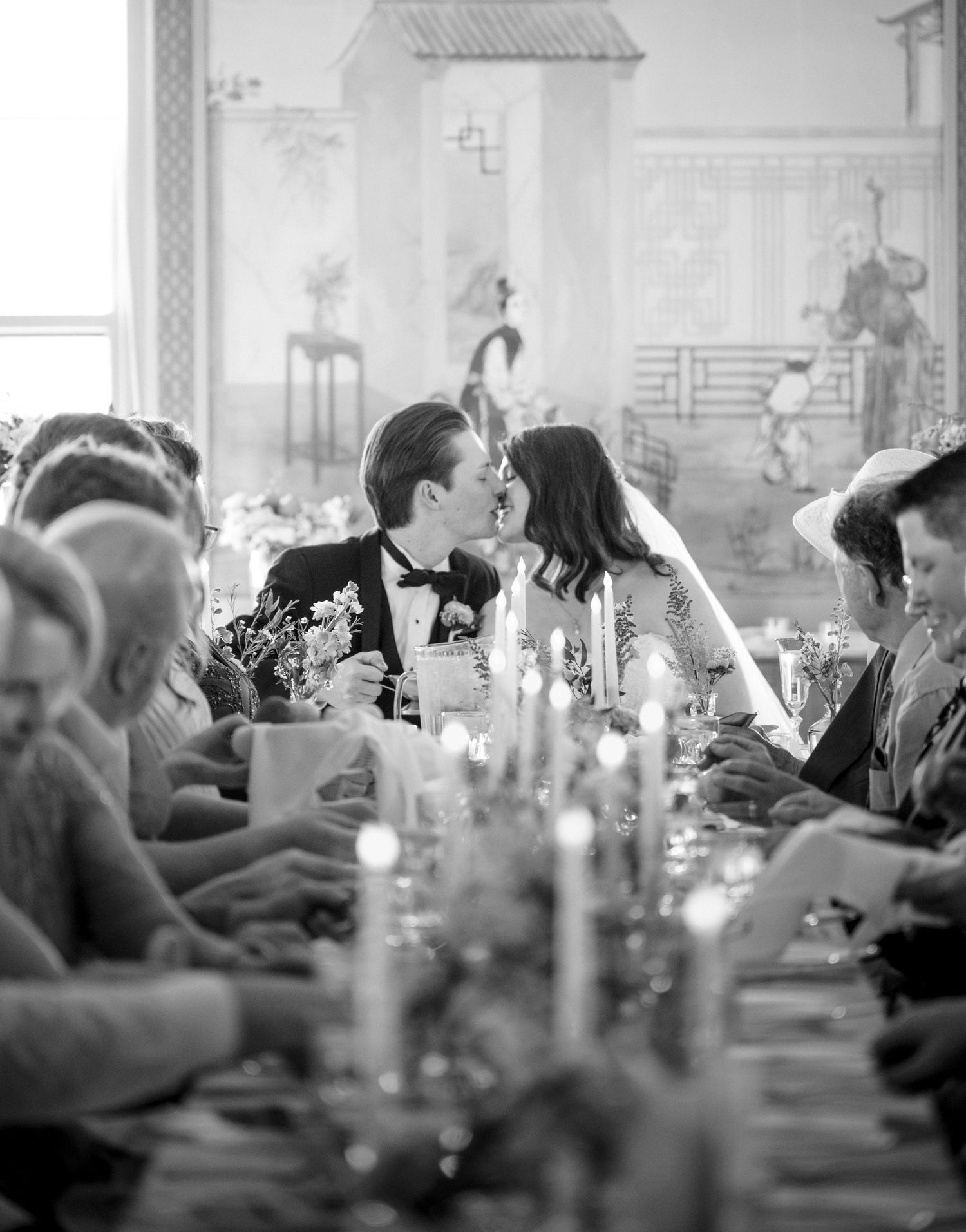 black and white photo of table and bride and groom kissing at end