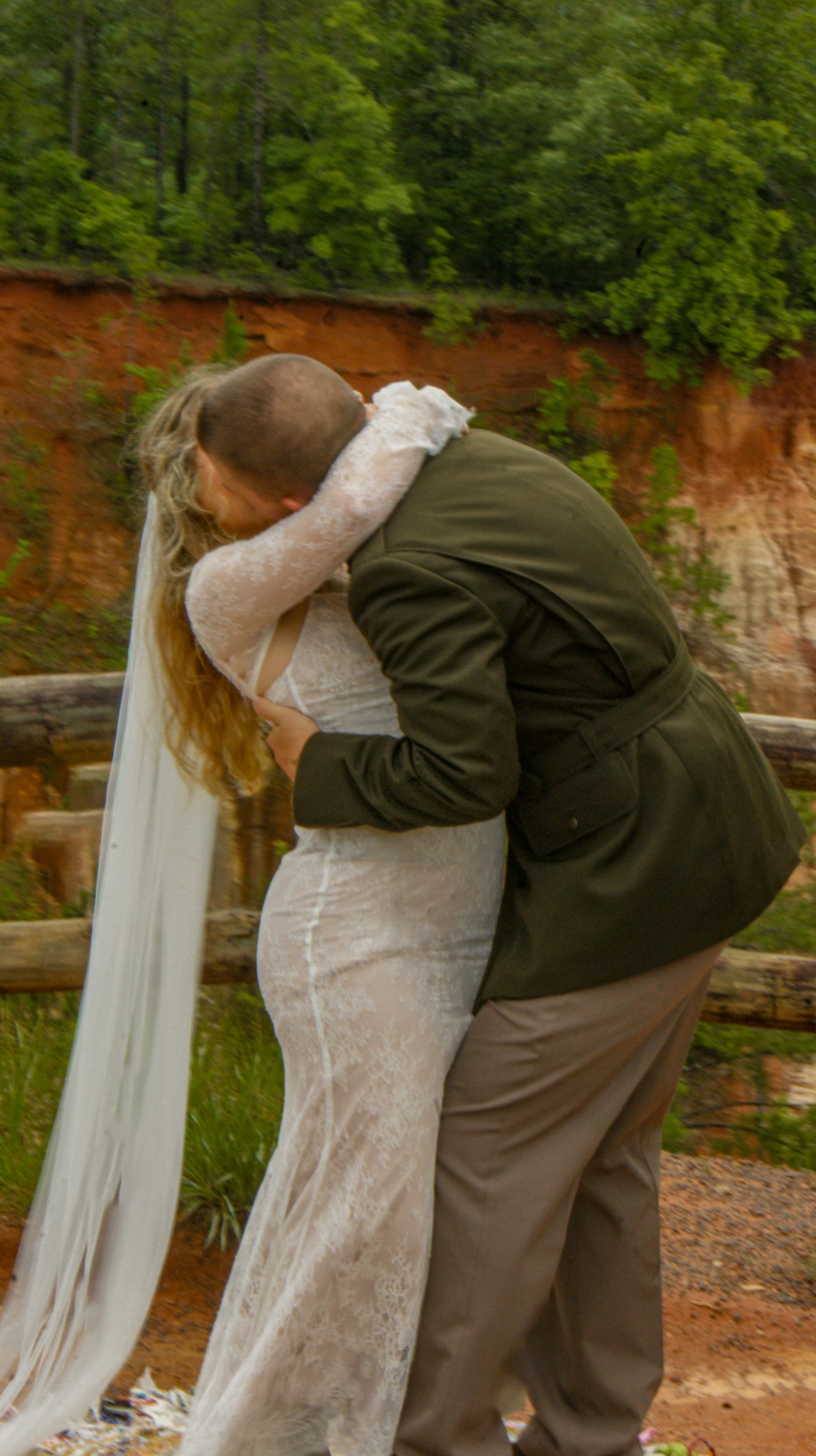 A couple embraces during their wedding ceremony against a backdrop of red clay cliffs.