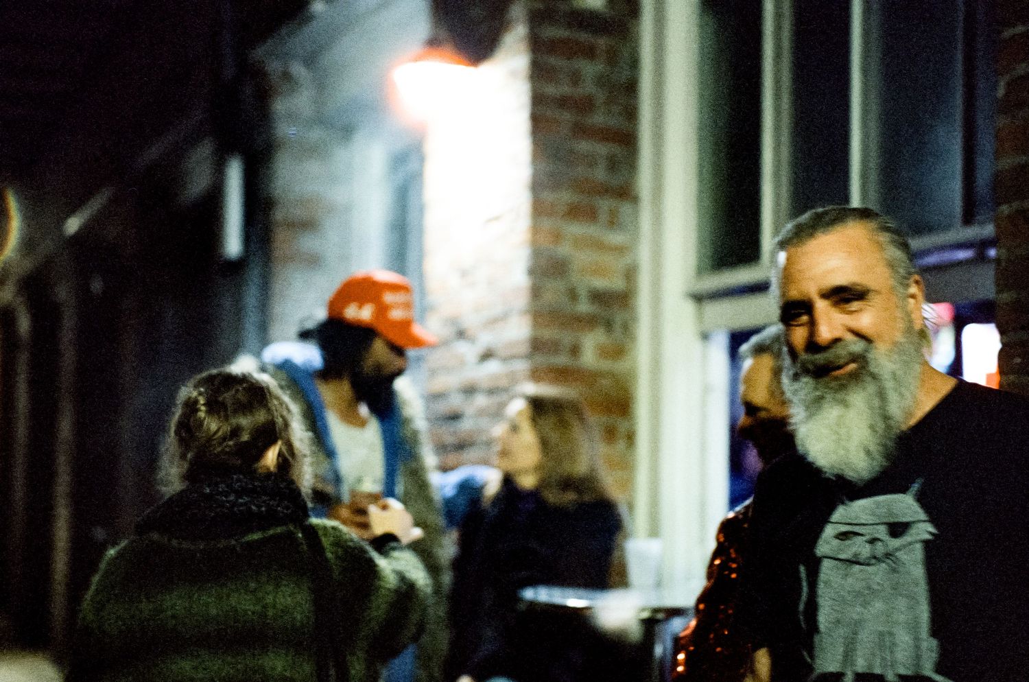 Nighttime gathering of people socializing outside a brick building.