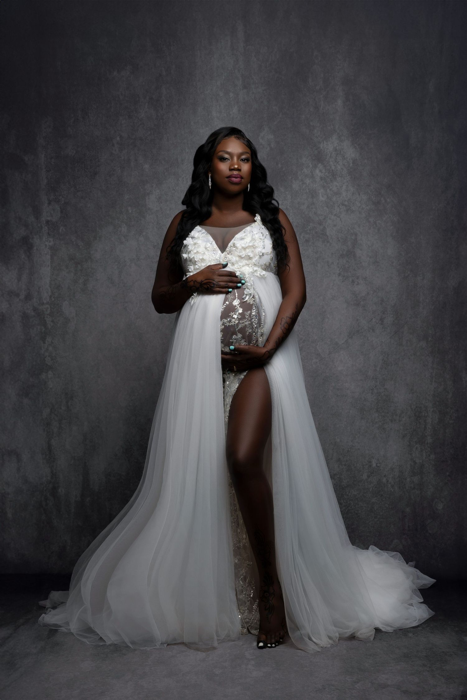 Elegant maternity photo featuring a flowing white gown with sequin details against a dark textured backdrop.