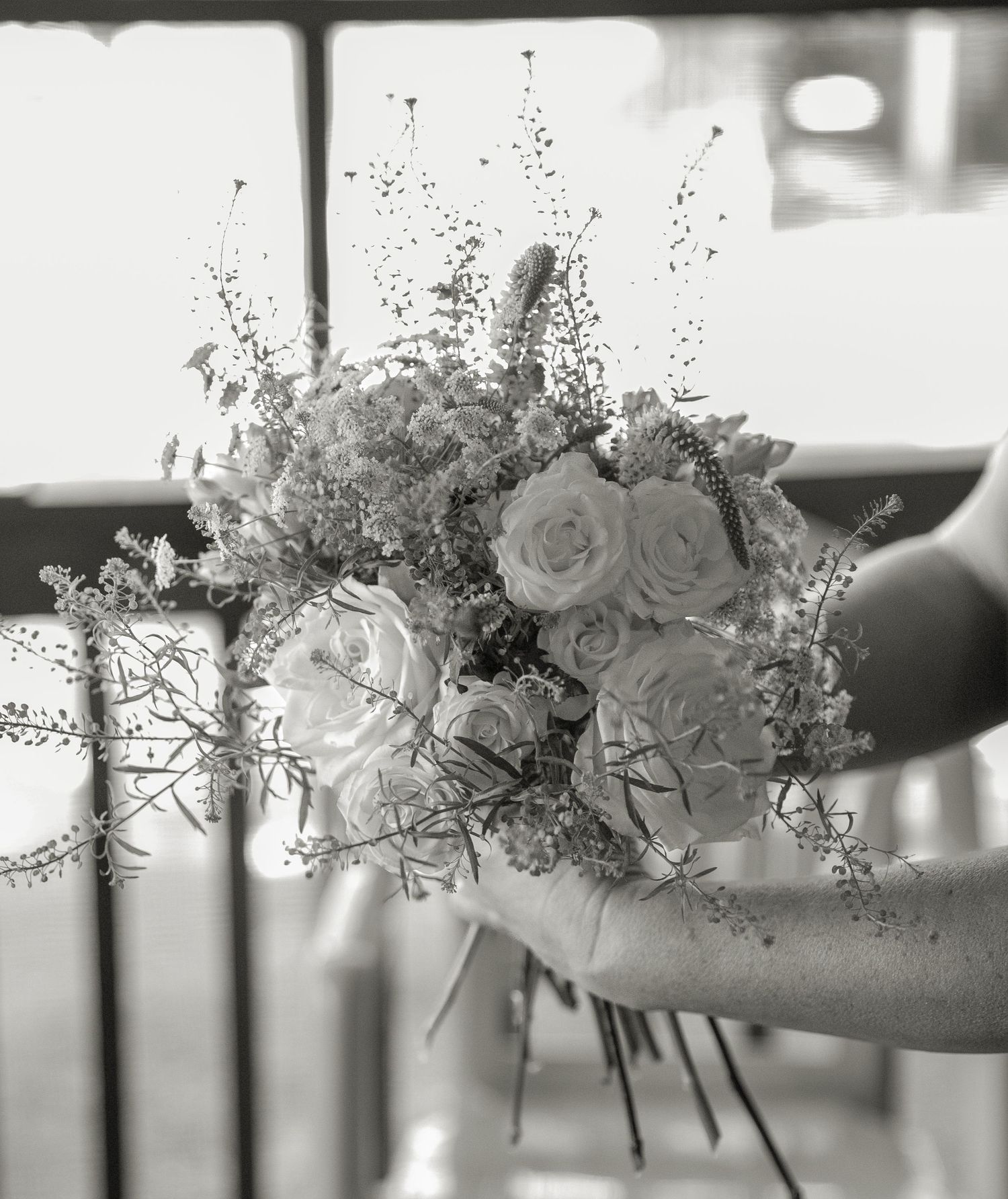 Black and white close-up of hand holding a beautiful bouquet of roses and wildflowers.