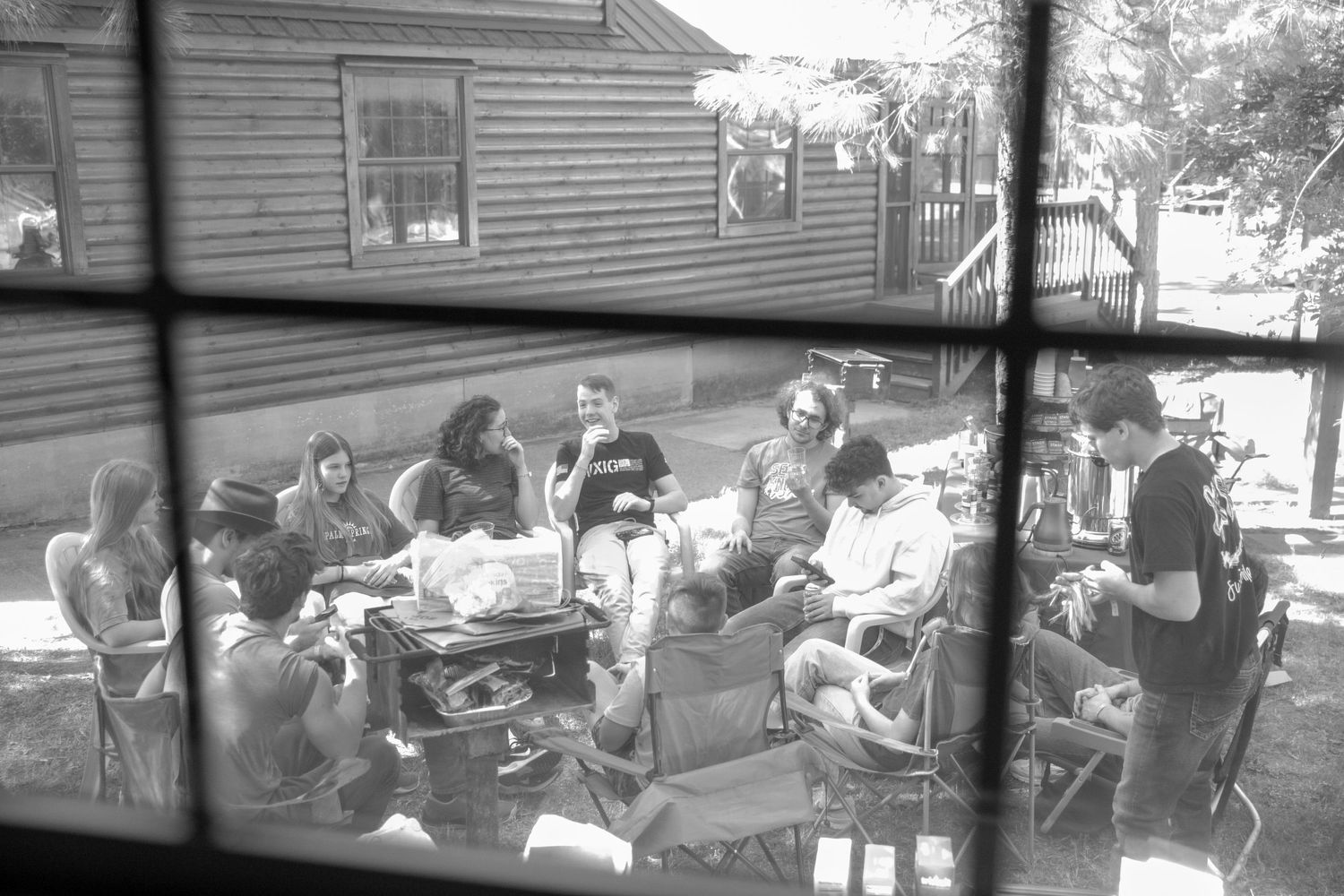 Black and white view through window of group gathered on outdoor patio.