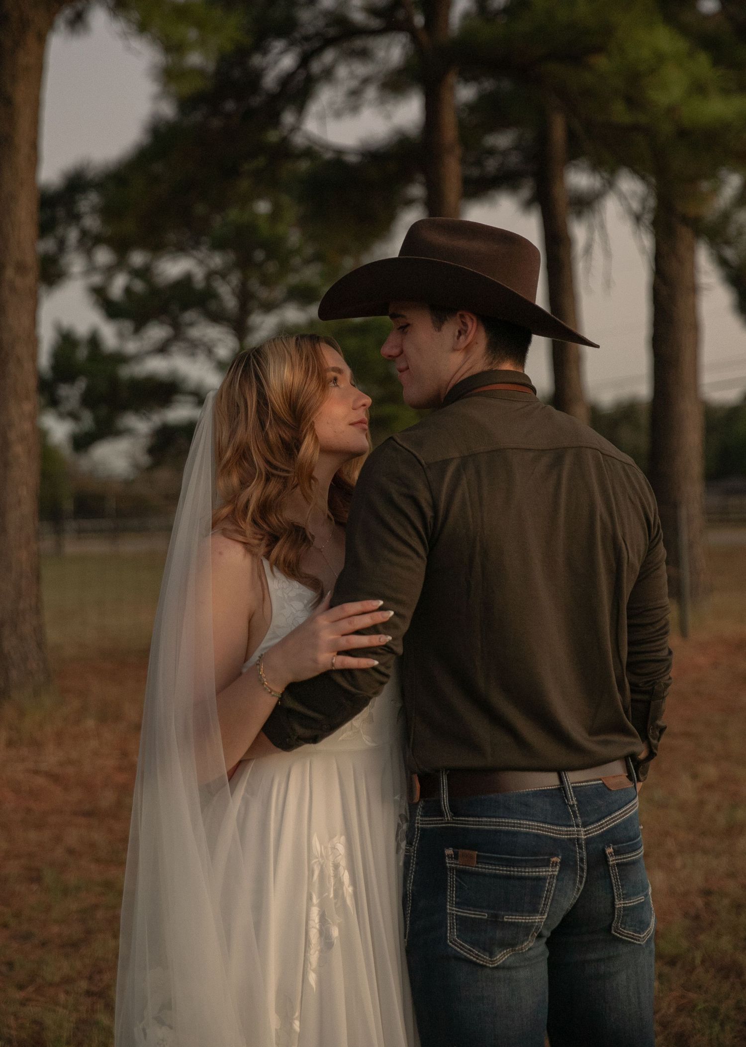 Bride and groom in cowboy hat sharing a romantic moment among pine trees at a rustic outdoor wedding.