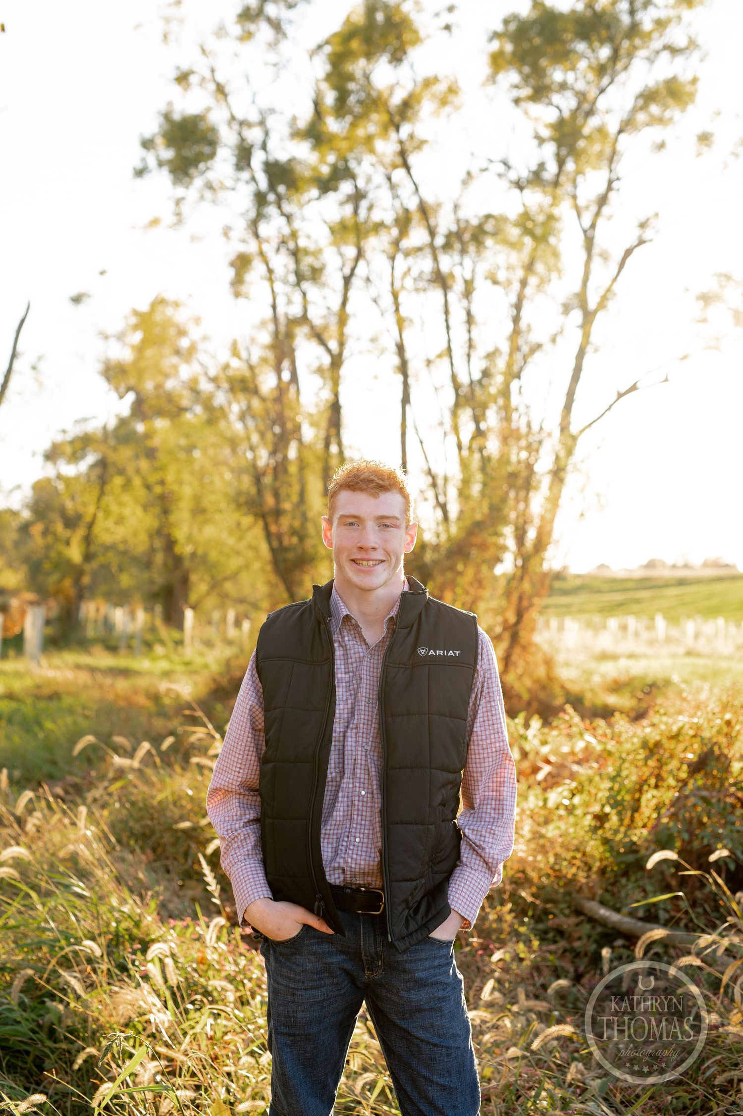 Casual autumn portrait in nature wearing dark vest and plaid shirt with trees in background.