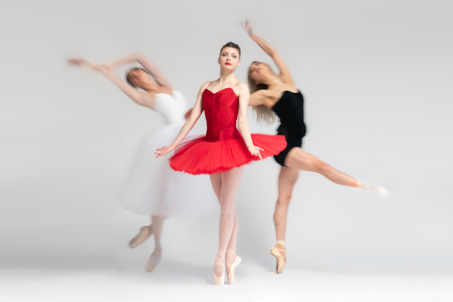 Ballet dancers in tutus performing synchronized movements on white background.