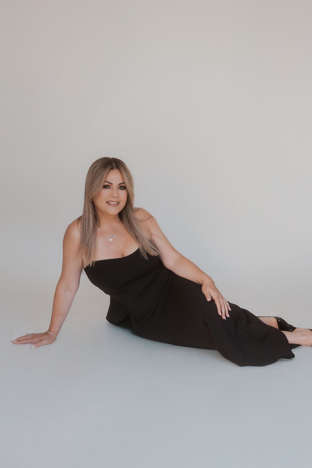 Woman in black formal dress reclines gracefully on studio floor during professional photoshoot.