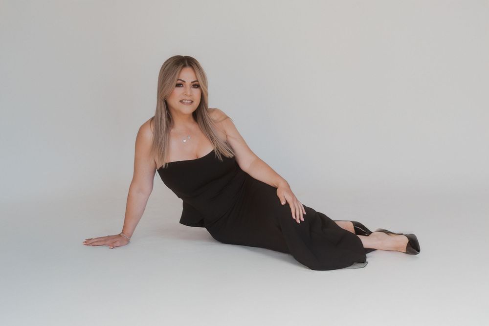 Woman in fitted black dress poses gracefully on floor during professional studio photoshoot.