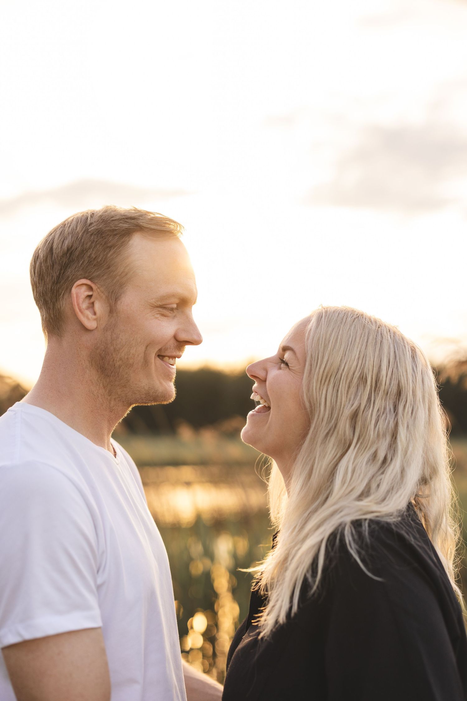 Par som står i solnedgången, tittar på varandra och skrattar.