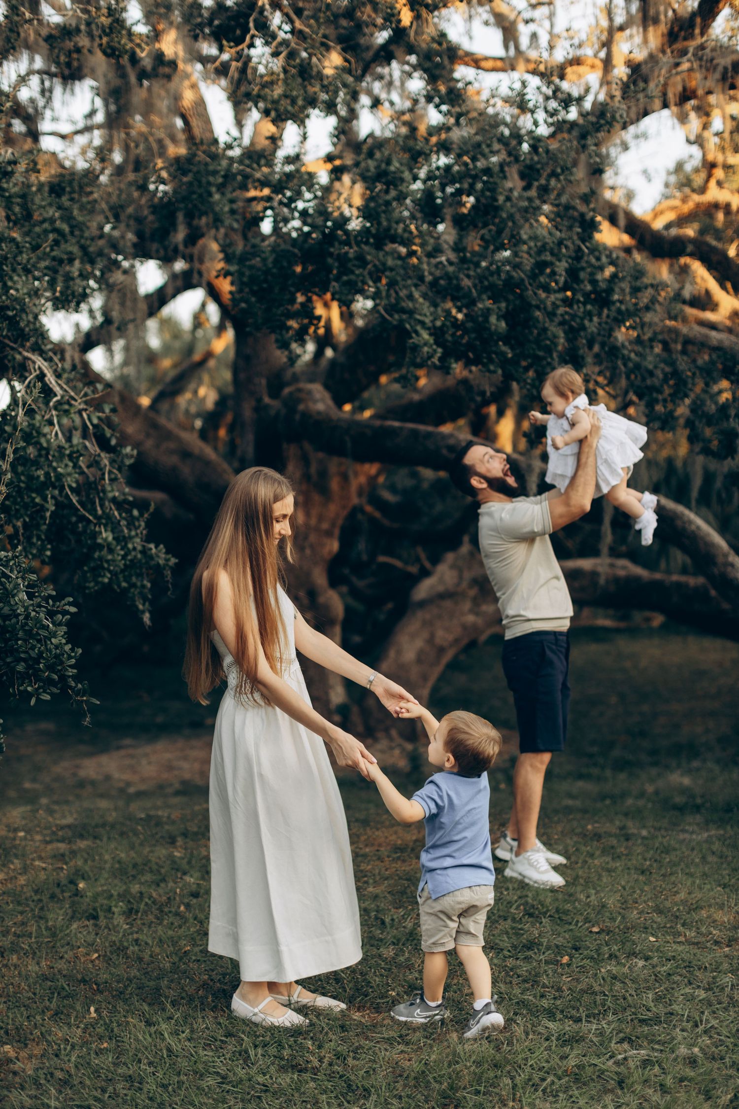 Family enjoying a playful moment under a large oak tree with Spanish moss.
