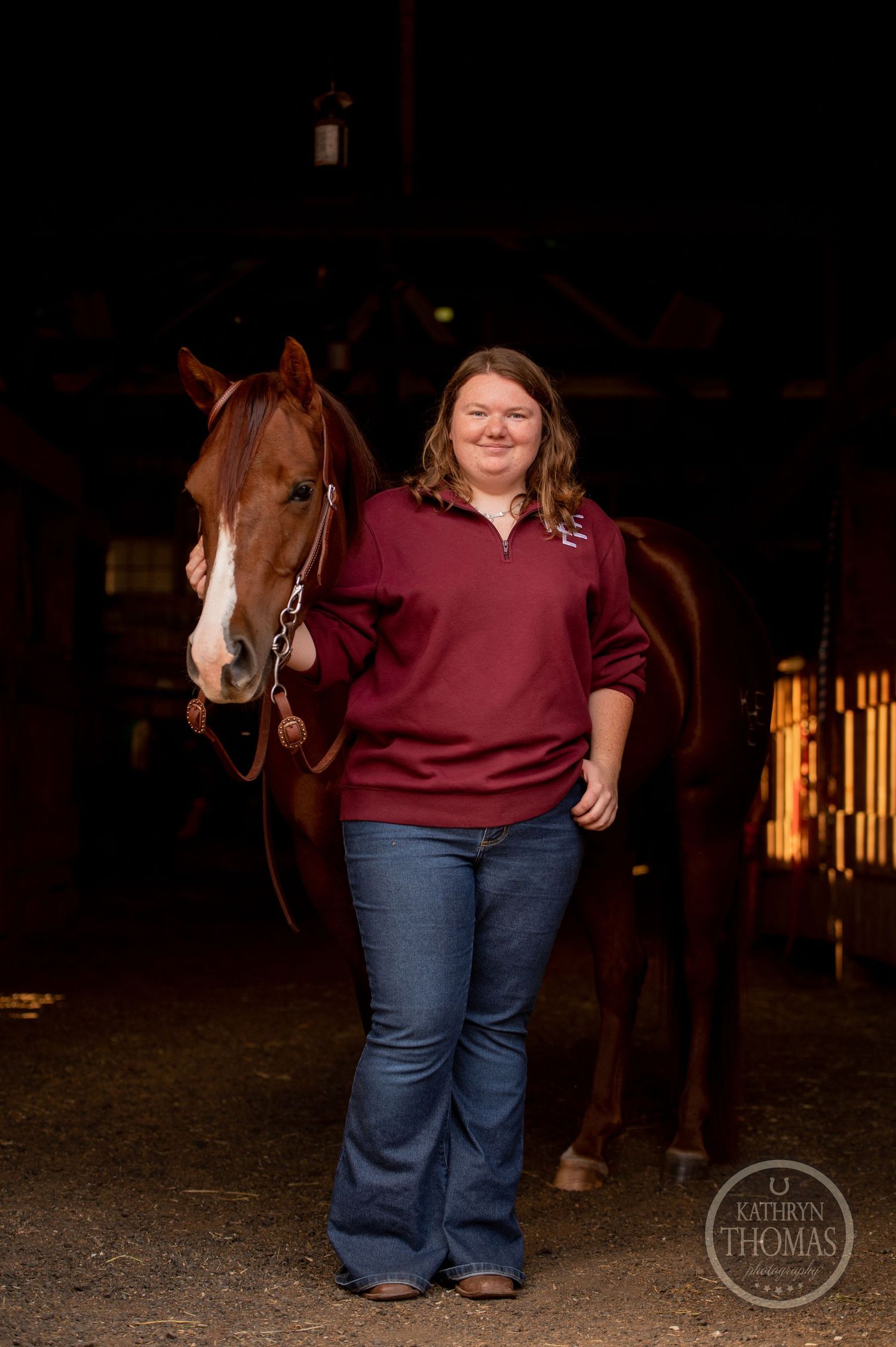 A chestnut horse and person wearing burgundy sweater stand together in a barn setting.