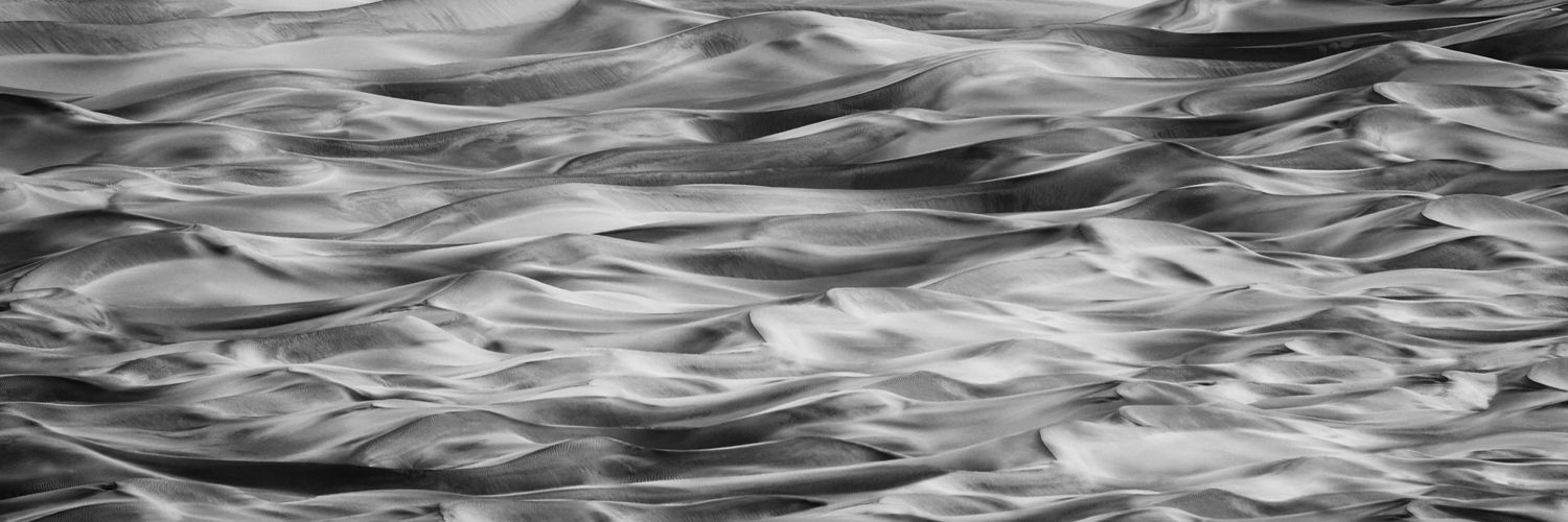 Abstract black and white sand dunes textured with smooth flowing waves and ripples creating a dynamic pattern.