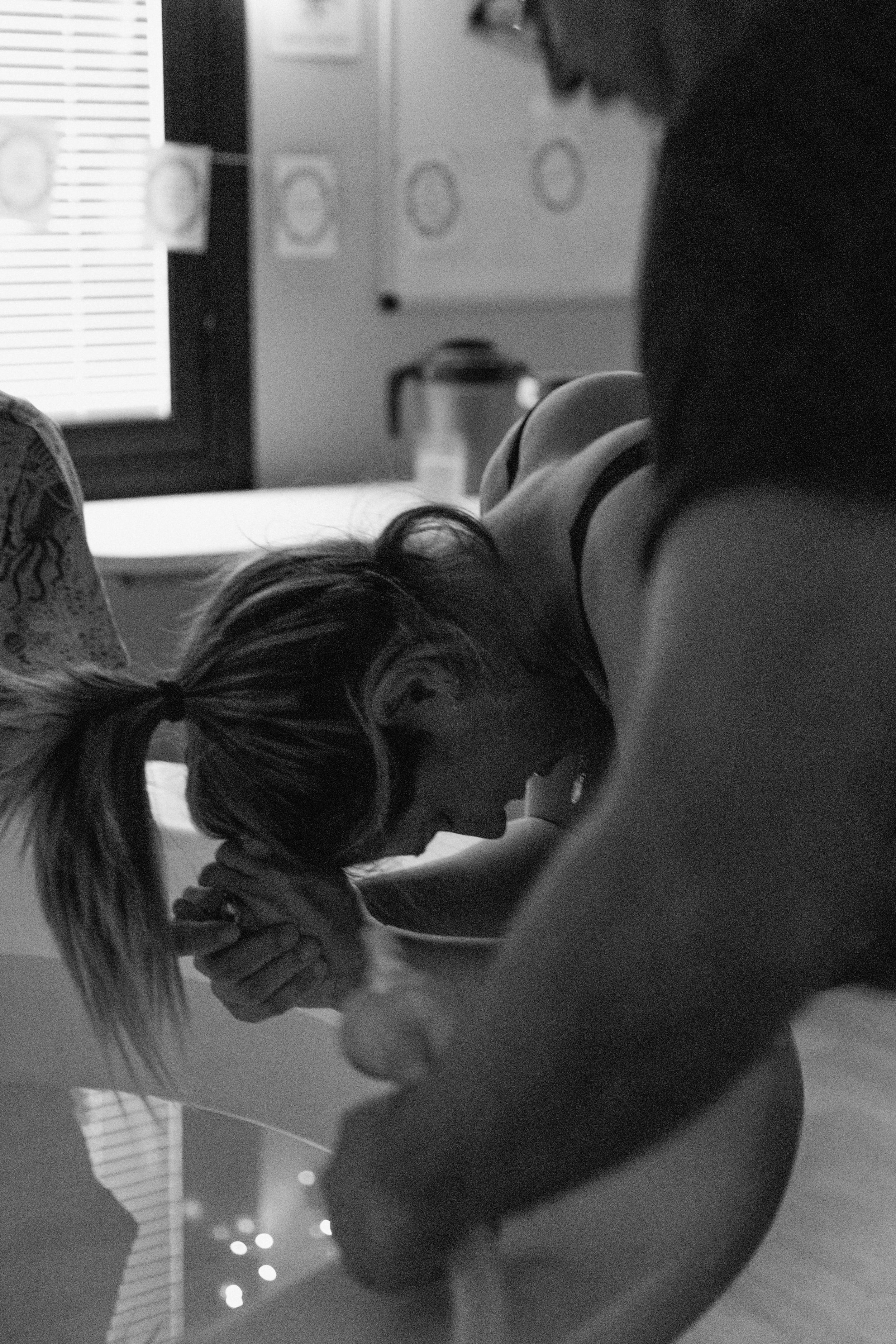A woman in labour leans on the edge of a tub during a contraction during a birth photography session, in Karratha, WA