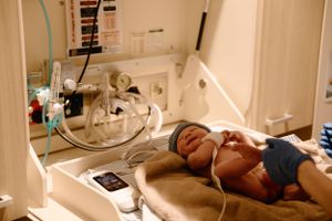 A newborn baby rests inside a hospital incubator with medical monitoring equipment. Birth photography, Karratha, WA