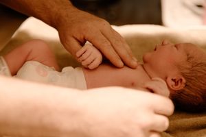 Adult hands tenderly hold a newborn baby lying on soft fabric during an intimate moment. Newborn photoshoot, Karratha