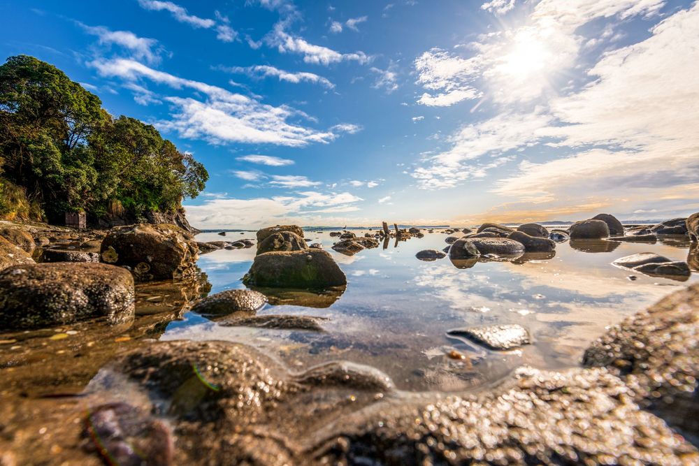 Rocky coastal landscape with dramatic cloudy sky reflecting in tidal pools at sunset along a rugged shoreline.