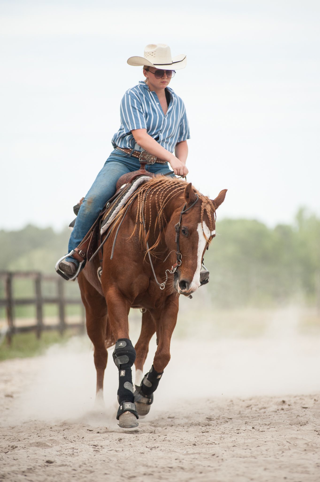 A western-styled pageant queen in blue paisley shirt and jeans holds a lasso at a ranch.