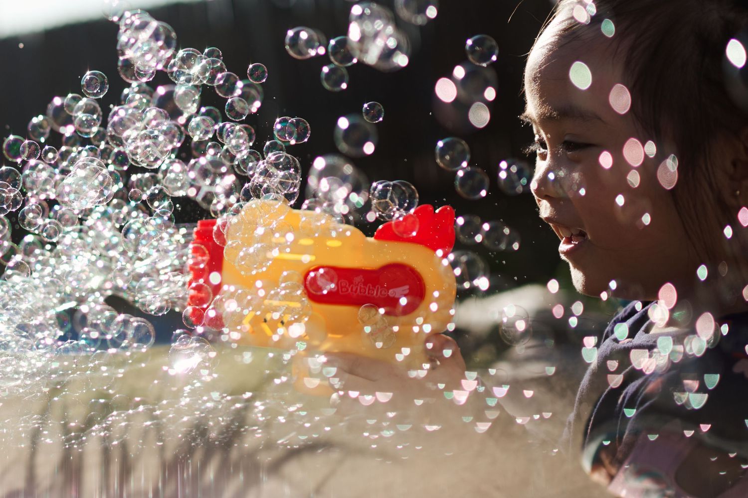 A yellow and orange bubble gun spraying bubbles in the background against a dark backdrop with a little girl smiling in Weston Ranch CA