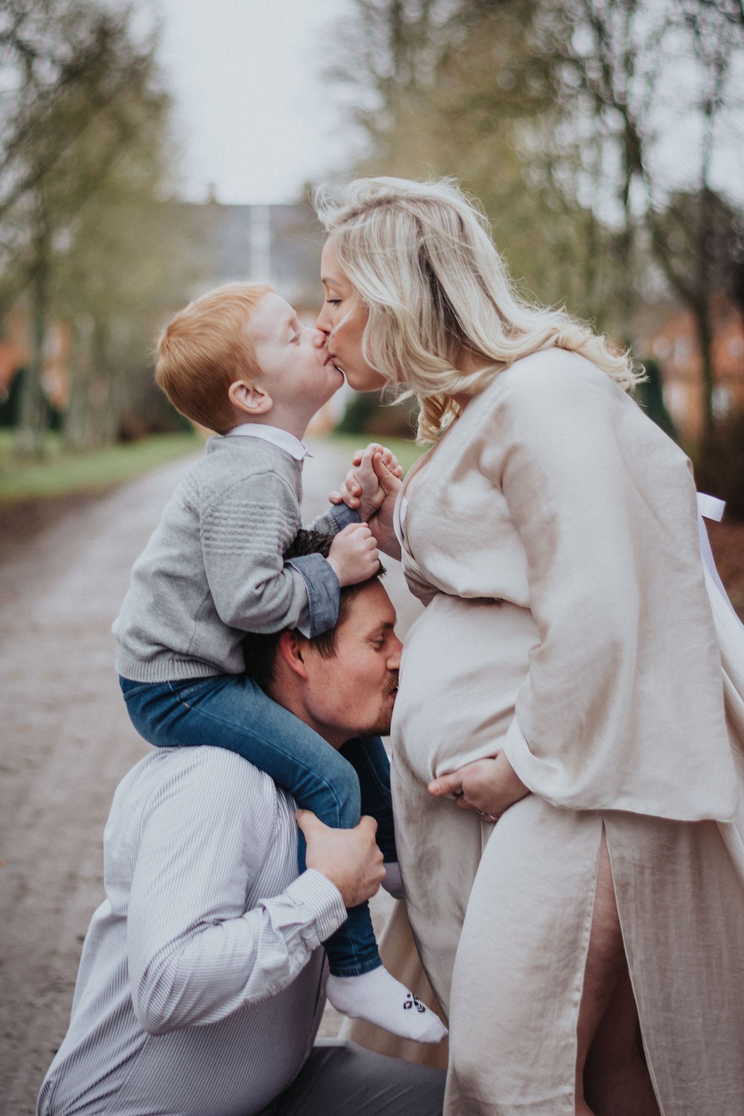 Tender family moment captured outdoors on path with autumn trees.