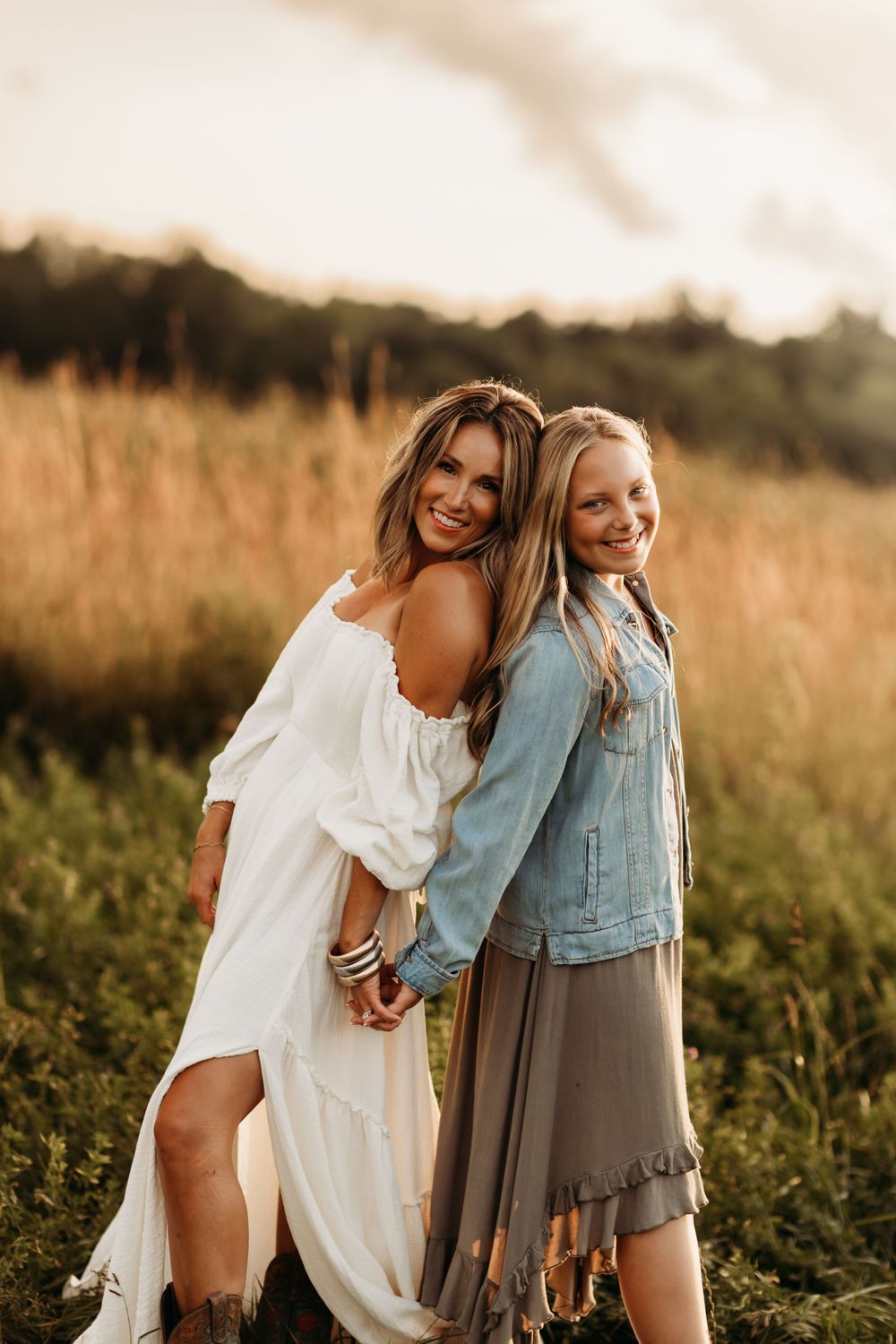 Mother and daughter pose together in a golden field during sunset wearing white and denim outfits.