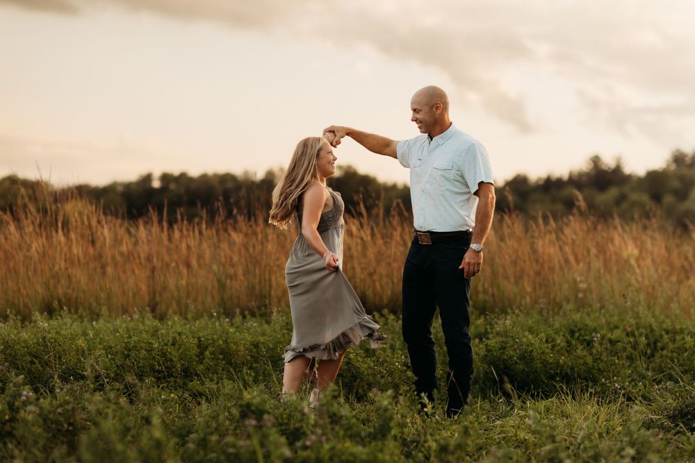 A Father and Daughter dances together in tall grass during a warm summer sunset.