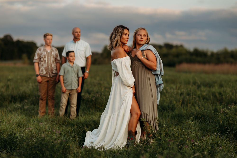 A romantic sunset photoshoot in a grassy meadow with people posing together in casual and formal attire.