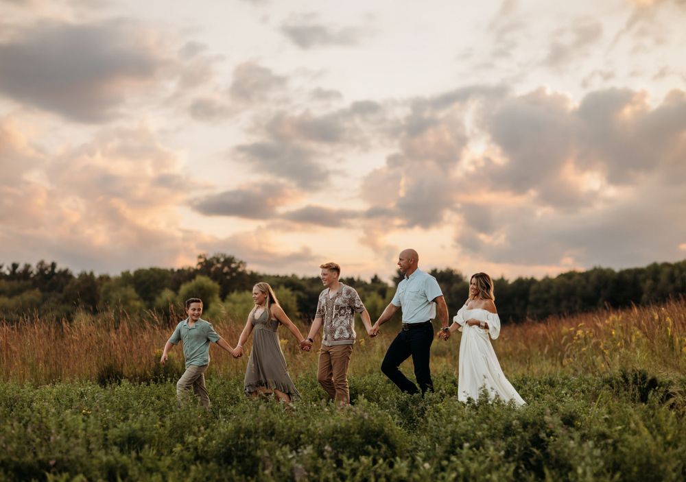 Family walking together through a golden field at sunset with dramatic cloudy sky.