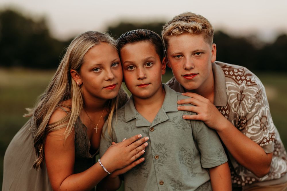 Close-up portrait of three people embracing in warm evening light.