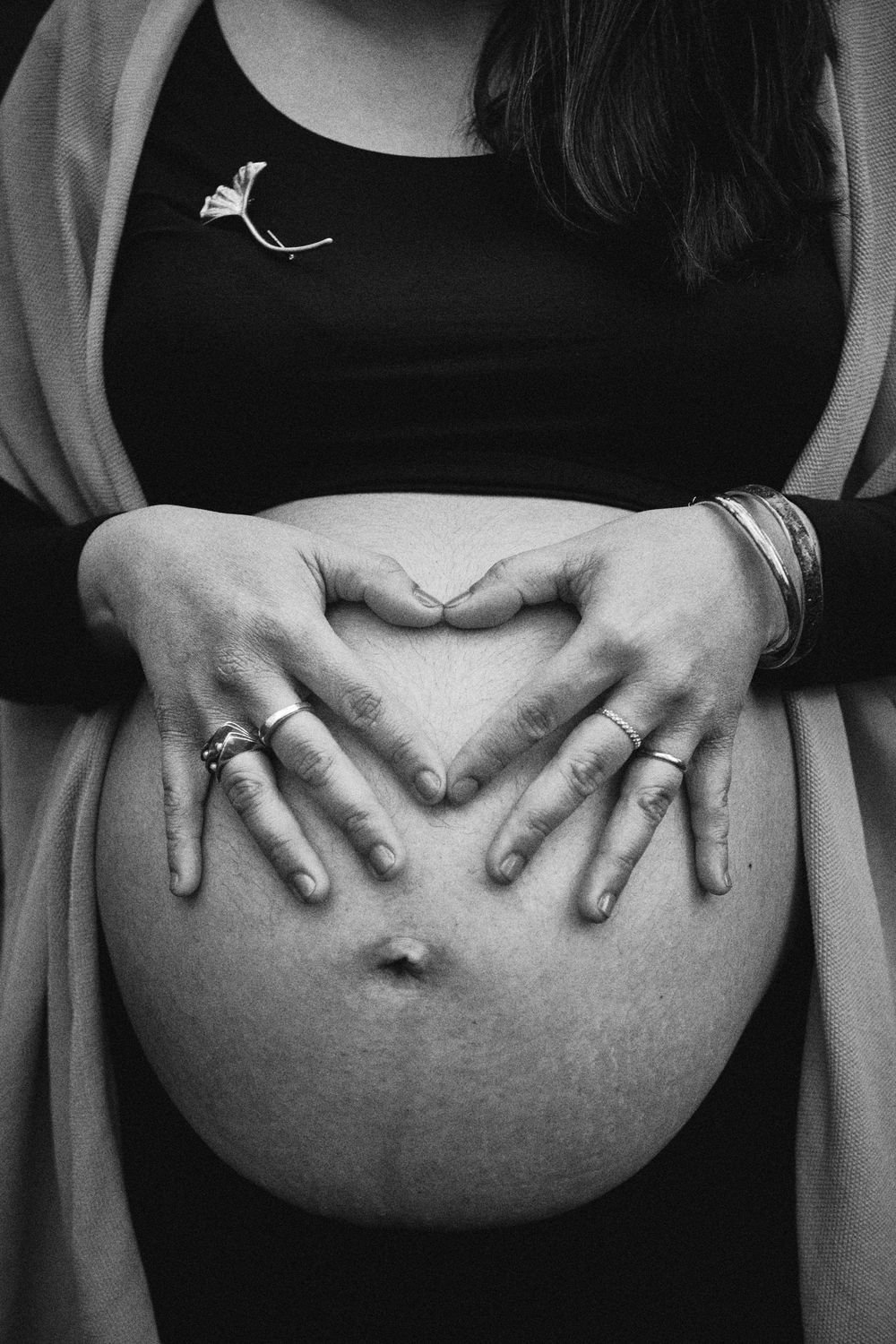 Black and white close-up of pregnant woman forming heart shape on bare belly.