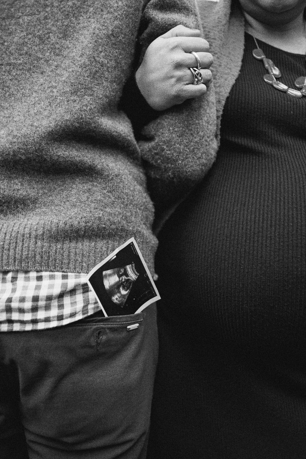 Black and white close-up of a couple with ultrasound photo tucked in pocket.